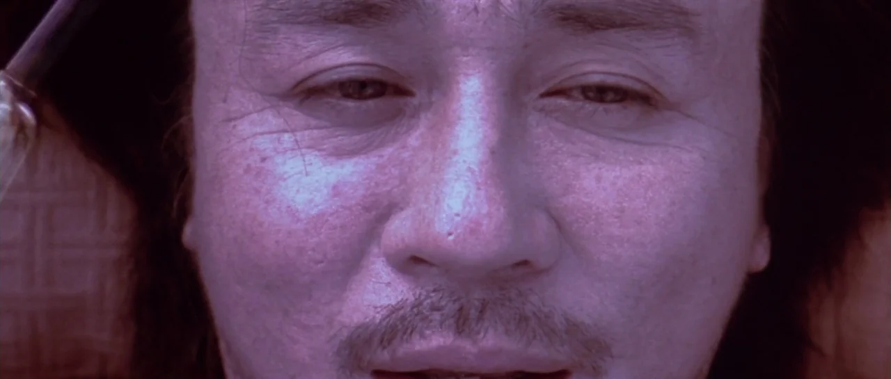 Oldboy (2003) movie still: closeup — A man's face fills the frame in a close-up against a textured background. The subject maintains a steady gaze…