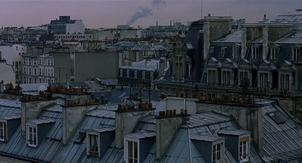 Vendredi Soir (2002) movie still: establishing — A dense urban landscape of zinc rooftops and stone chimneys stretches toward the horizon. The…