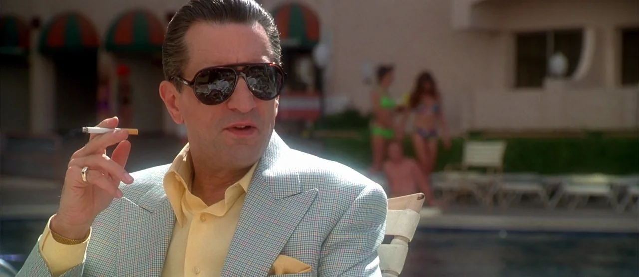 Casino (1995) movie still: medium — A sunny pool deck at a hotel features blurred figures in swimwear in the background. A man in a pastel plaid…