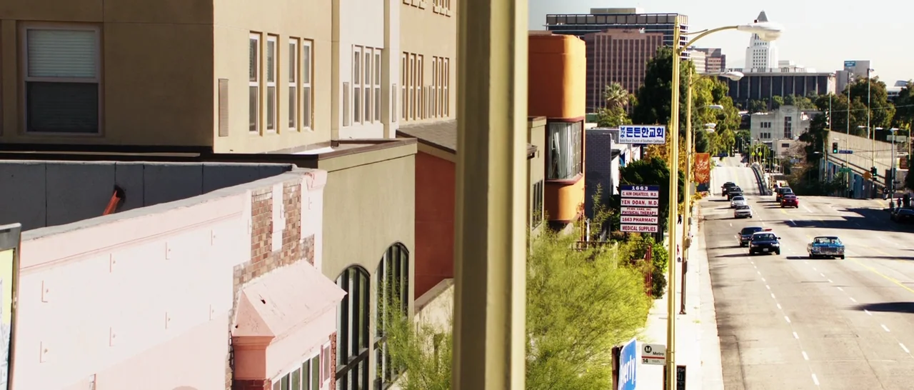 Rampart (2011) movie still: establishing — A view from an elevated vantage point overlooking a multi-lane city street. Buildings of varying…