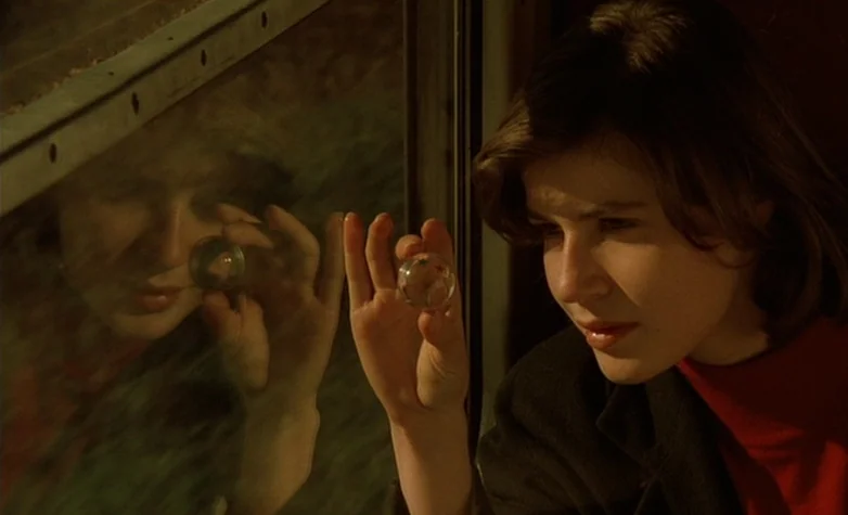 The Double Life of Véronique (1991) movie still: closeup — A woman looks through a glass marble against a train window pane. Her reflection is…