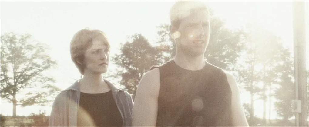 Minority Report movie still: medium — A bright outdoor scene features a man and a woman standing in a field. Intense sunlight from behind washes out…