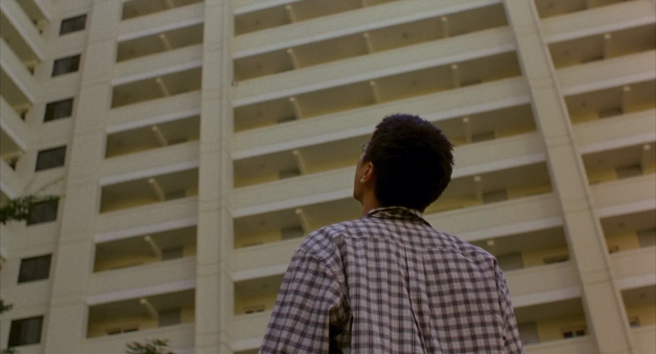 Barking Dogs Never Bite (2000) movie still: medium — A multi-story beige apartment complex rises high into the frame with repetitive balconies. A…