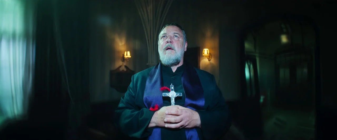 The Pope’s Exorcist (2023) movie still: medium — An interior space with arched architecture features a man wearing a clerical collar. The man stands…