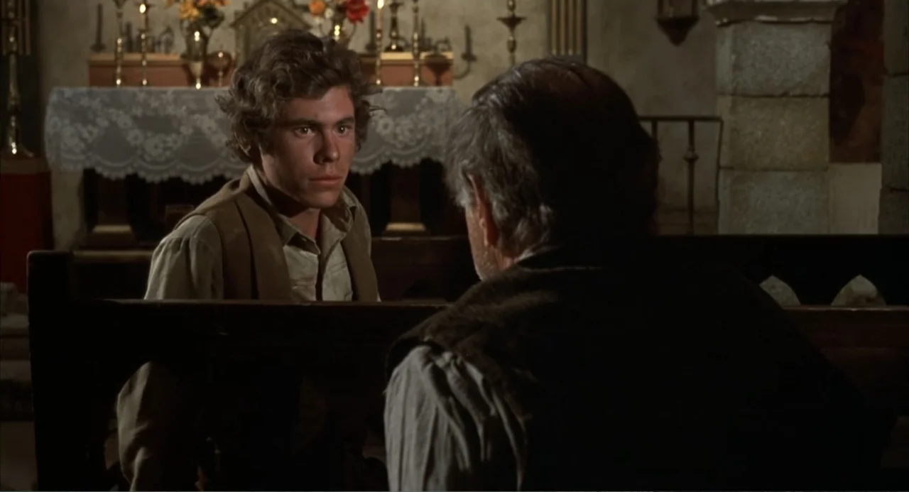 The Spikes Gang (1974) movie still: medium — A stone church interior features a wooden pew and an altar in the background. A young man sits opposite…
