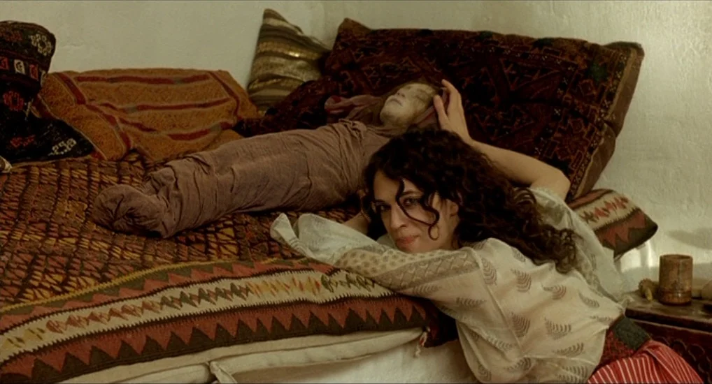 The Last Mistress (2007) movie still: medium — A rustic interior features a bed covered with various traditional woven patterned blankets and…