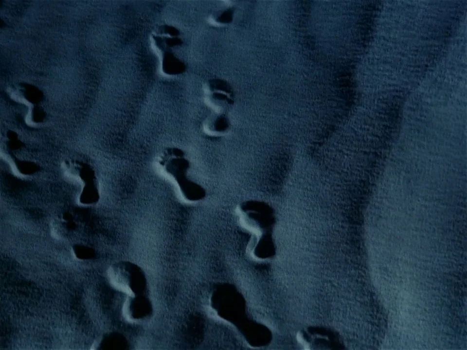 One From The Heart (1982) movie still: establishing — A vast expanse of fine-grained sand at night features multiple sets of human footprints. The…