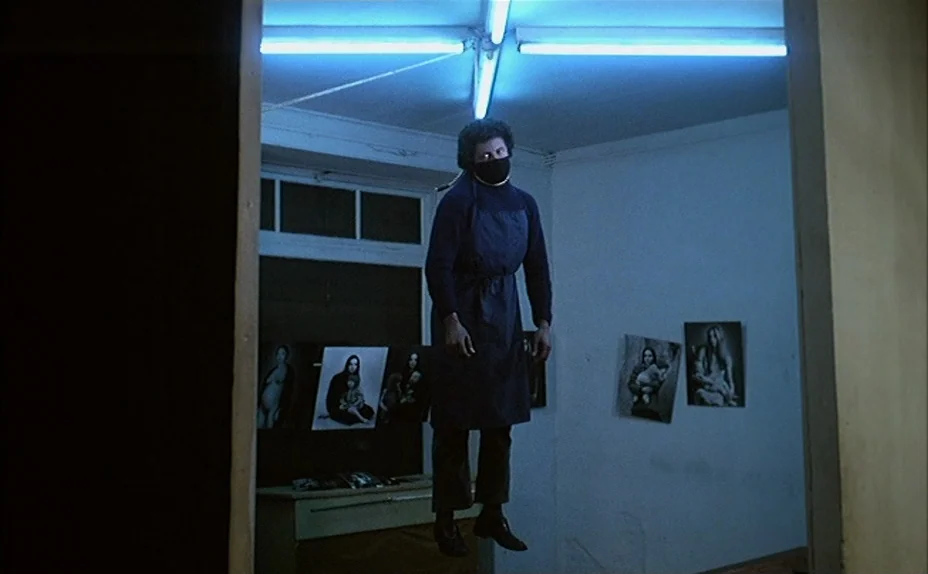 L’une Chante, l’Autre Pas (1977) movie still: fullbody — A spare interior space with blue-tinted walls is decorated with several framed…