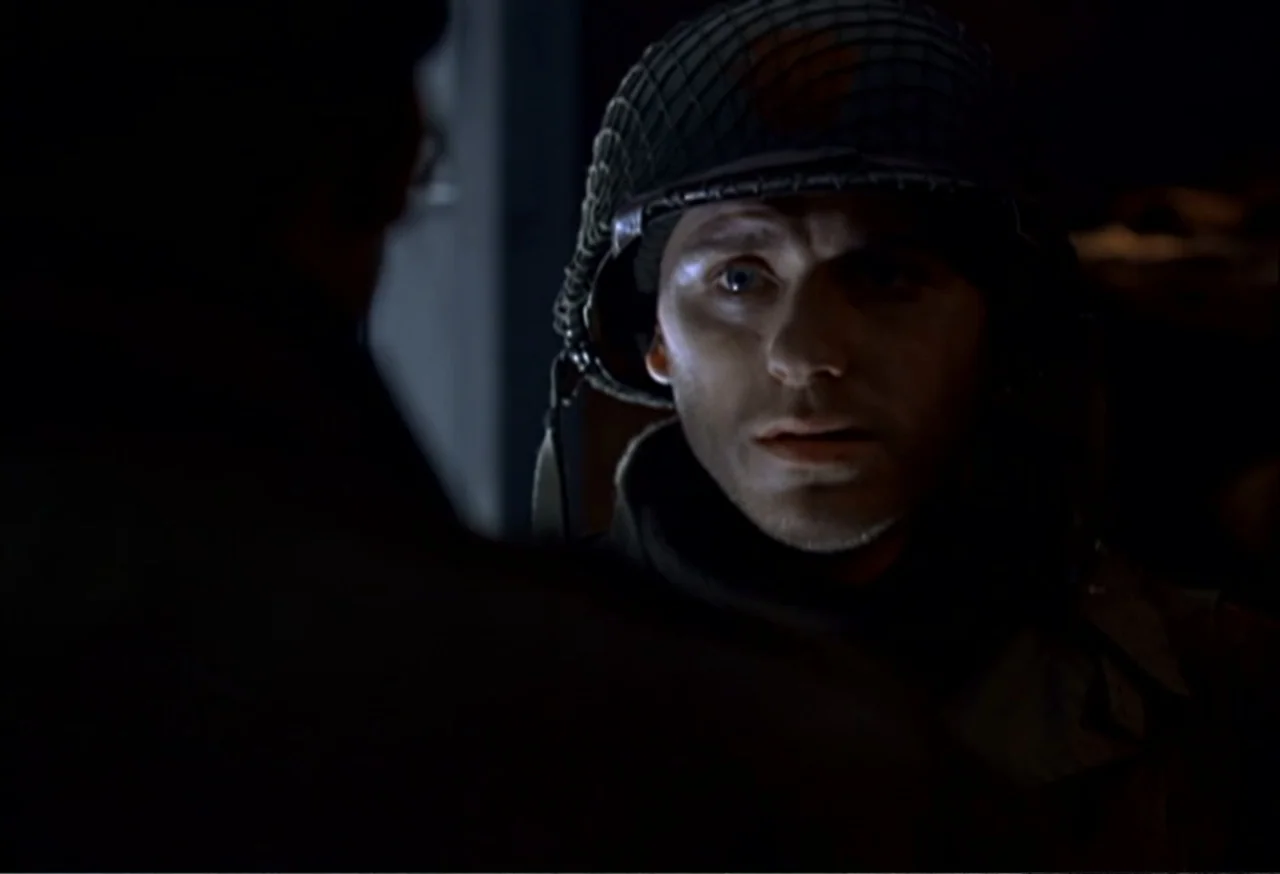 When Trumpets Fade (1998) movie still: closeup — A dimly lit interior space with shadows obscuring the surroundings. A young male soldier wearing a…