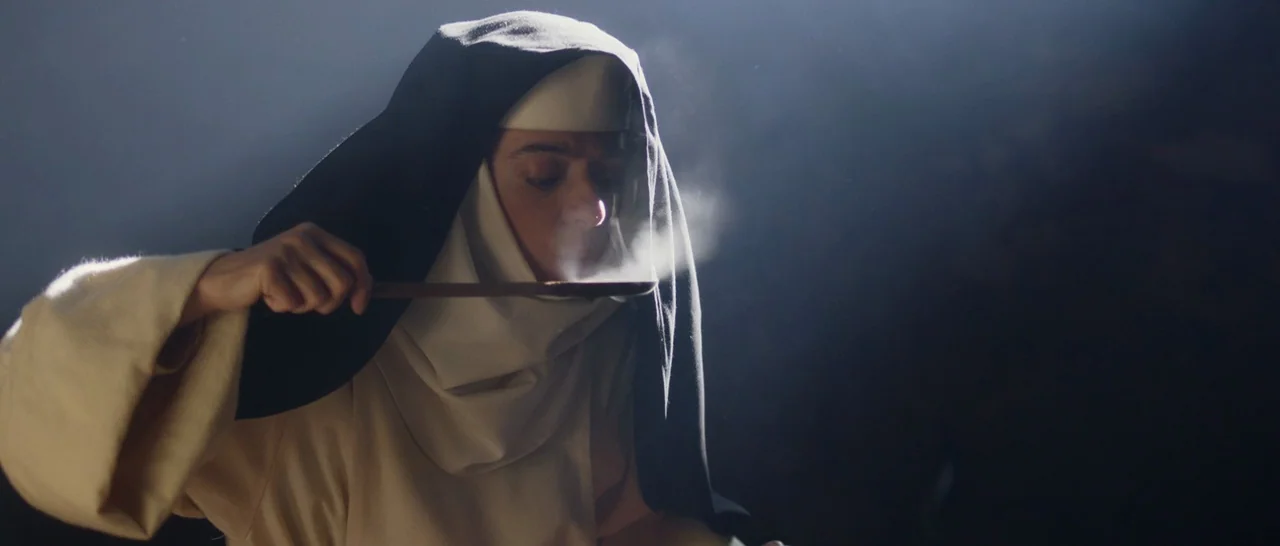 The Little Hours (2017) movie still: closeup — A dimly lit room serves as the setting for the subject. A woman in a religious habit holds a spoon…