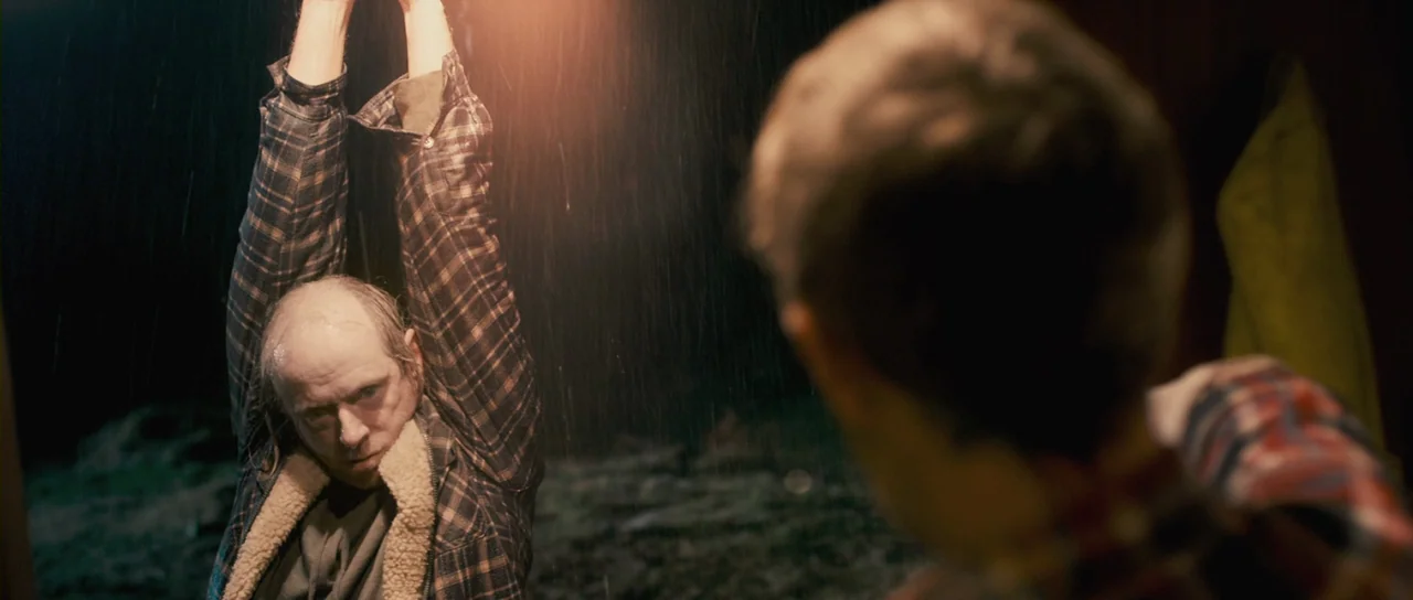 Grabbers (2012) movie still: medium — An outdoor night environment during a heavy rainstorm with darkness surrounding the subjects. A bald man in a…