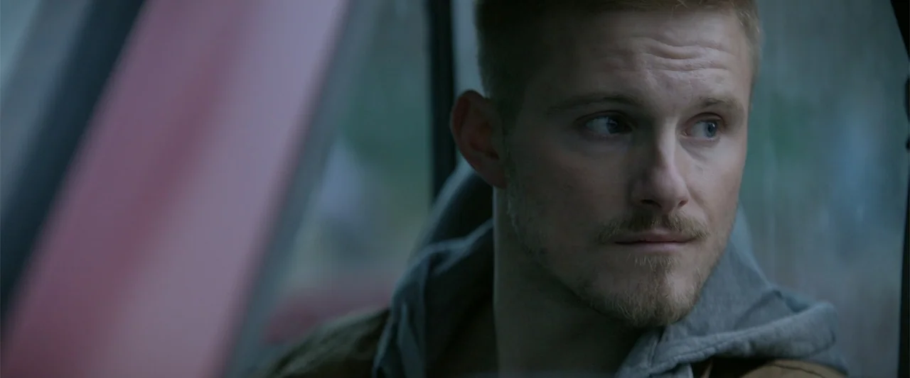 Marked Men: Rule + Shaw (2025) movie still: closeup — A man sits inside a vehicle looking through the window at an unseen exterior. The cabin is…