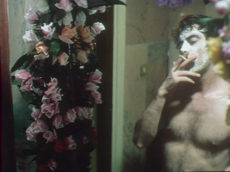 Hermitage (1968) movie still: medium — A man stands before a reflective surface partially obscured by a large floral arrangement. He holds a…