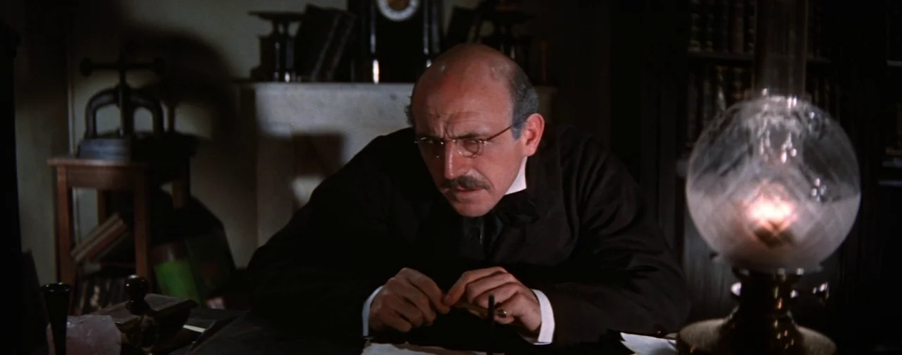 Lust For Life (1956) movie still: medium — A dimly lit room with bookshelves and a marble fireplace mantel visible in back. A bald man with glasses…