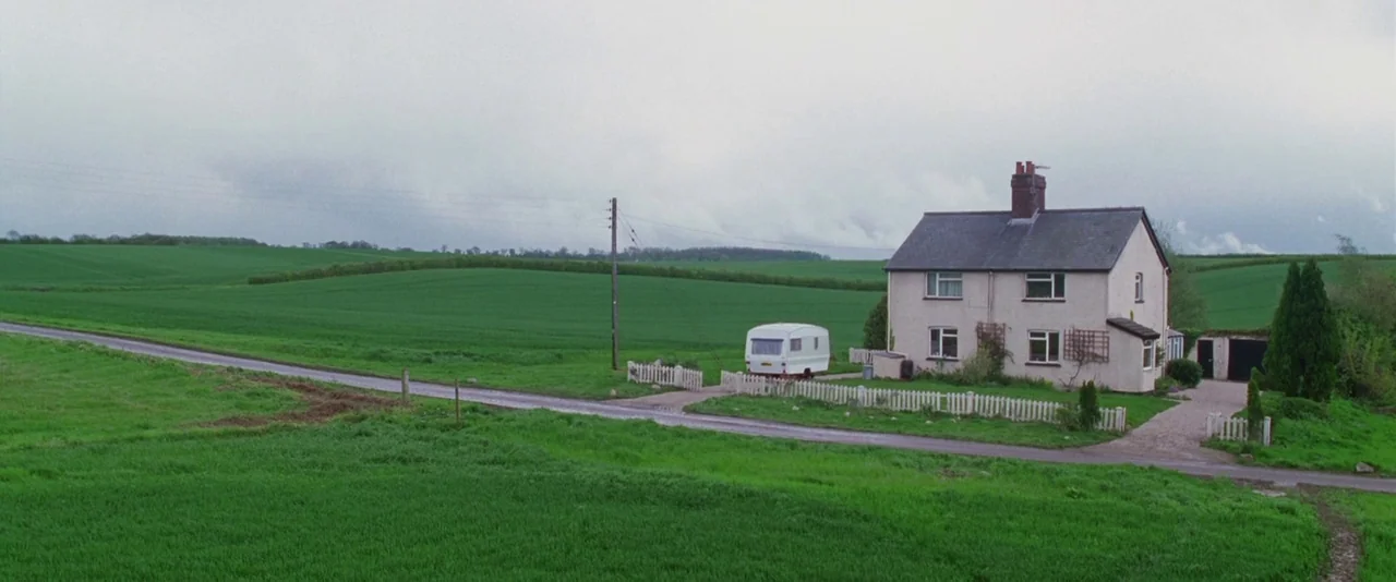 A Hitchhiker’s Guide To The Galaxy (2005) movie still: establishing — A detached house with a white picket fence sits amidst vast, rolling green…