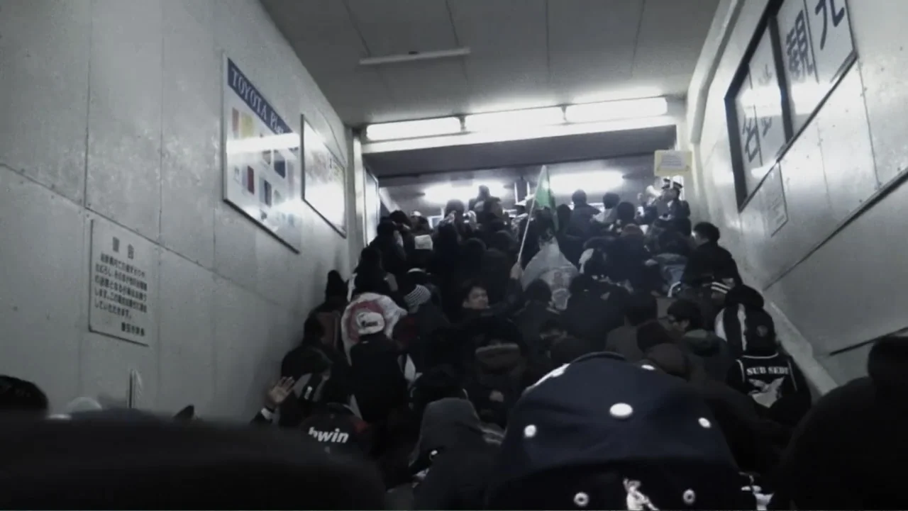 Vai Corinthians (2023) movie still: fullbody — A crowded subway stairwell features stark white tiled walls covered with framed public signage. A…
