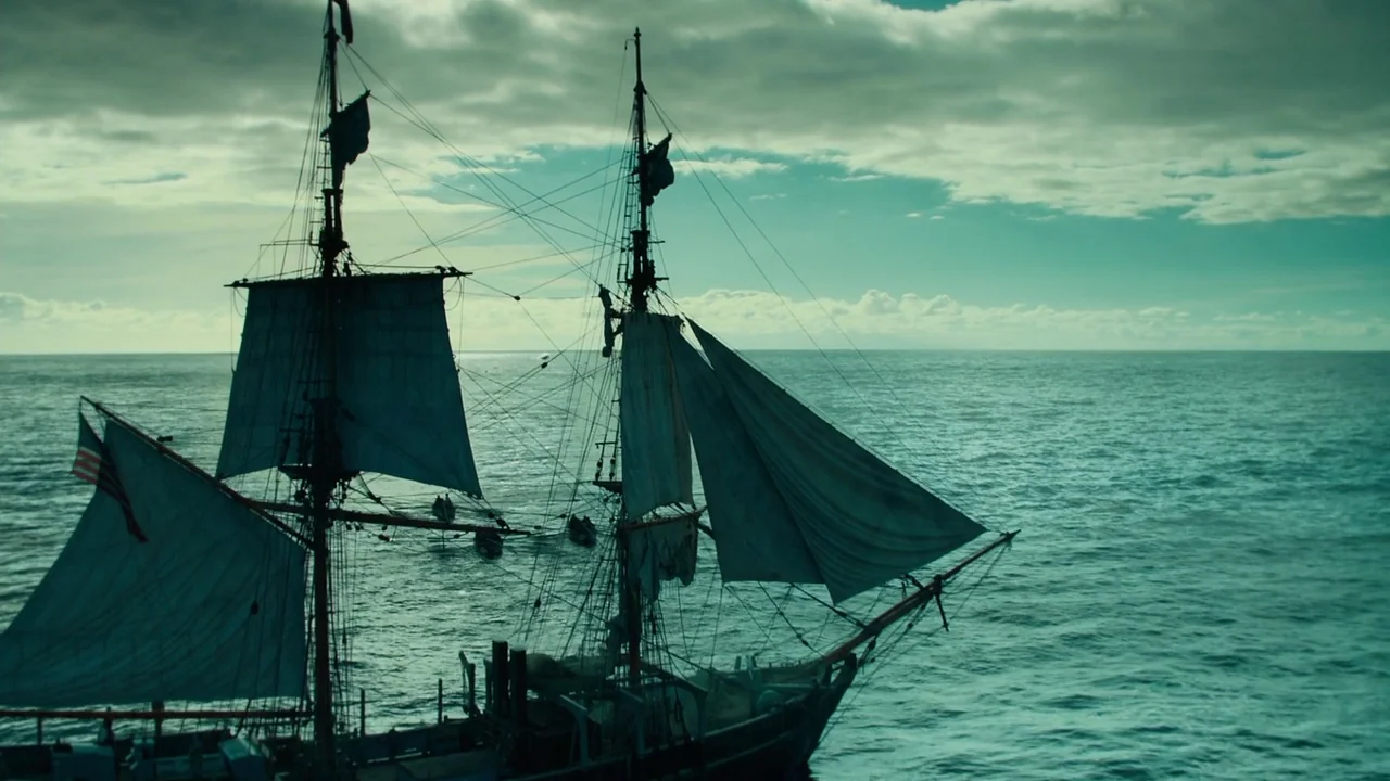 In The Heart of the Sea (2014) movie still: wide — An old-fashioned wooden sailing ship moves through a vast, calm ocean under cloudy skies. Small…