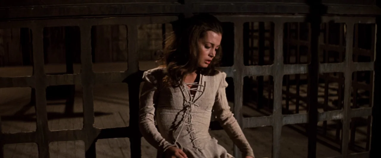 Westworld (1973) movie still: medium — A dark, textured metal lattice partition occupies the background of a dimly lit interior. A young woman with…