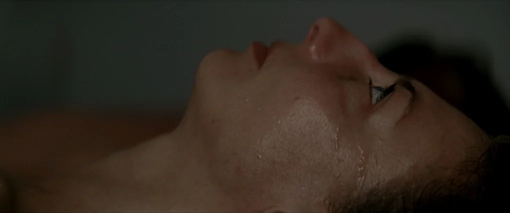 Silent Light (2007) movie still: closeup — A close-up view of a woman's face resting on a dark surface. Her skin is damp and she gazes upward with…