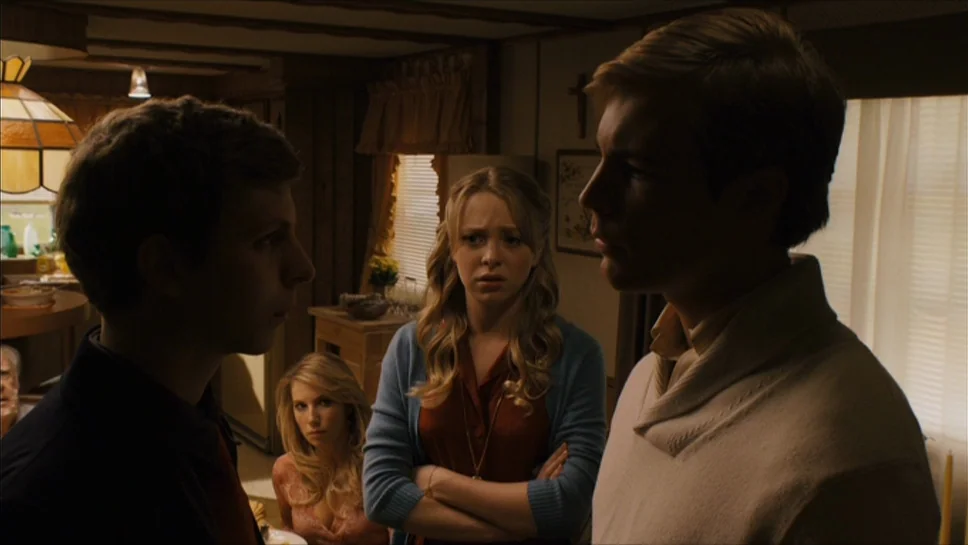 Youth In Revolt (2009) movie still: medium — A dimly lit room with wood-paneled walls and a traditional domestic aesthetic. Three young adults stand…