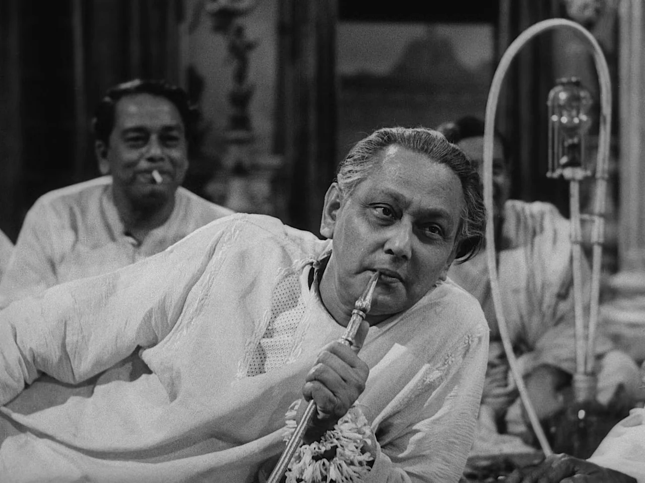 The Music Room (1958) movie still: medium — A dimly lit room with ornate, dark architectural details in the background. A man lies reclined while…