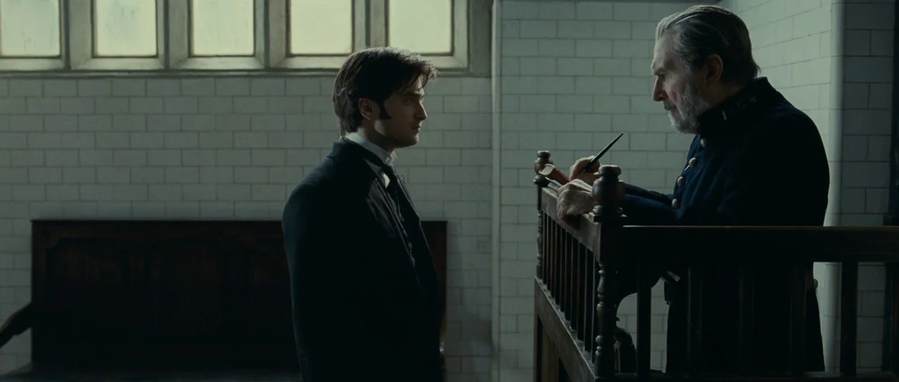 The Woman in Black (2012) movie still: medium — An institutional room features white tiled walls and high windows in a grid pattern. A man in a suit…