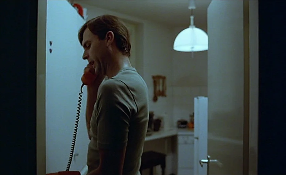 Possession (1981) movie still: medium — A man stands in a dark corridor holding a telephone handset to his ear. Behind him, a partially visible room…