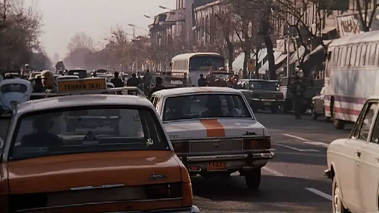 The Mirror (2014) movie still: wide — A dense urban thoroughfare with multiple vintage cars, taxis, and buses in heavy traffic. Pedestrians walk…