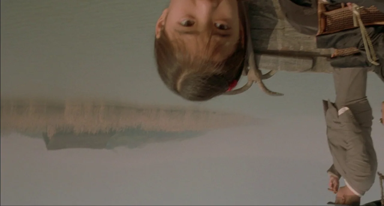 Shanghai Triad (1995) movie still: medium — A wooden dock extends over calm water with a distant hazy landmass visible. A young girl and a man stand…