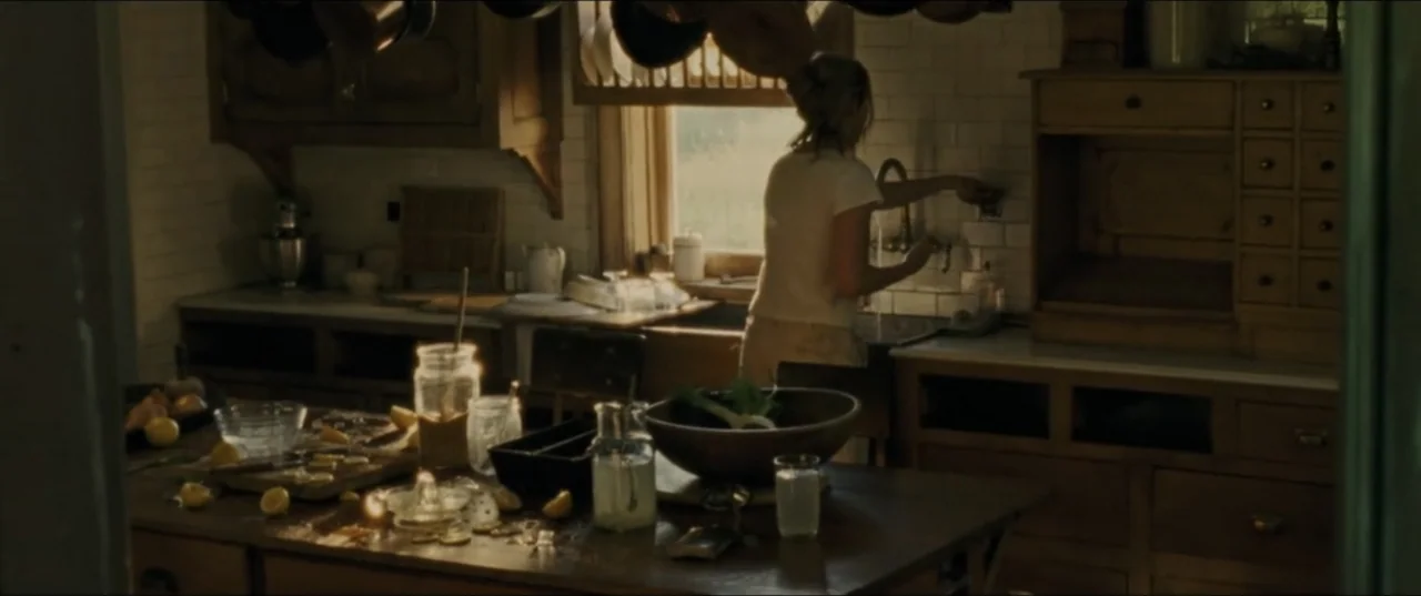mother! (2017) movie still: medium — A rustic kitchen features dark wooden cabinetry and a large central island. A woman faces away from the camera…