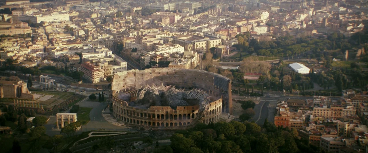 Godzilla x Kong: The New Empire (2024) movie still: establishing — An aerial view of the Roman Colosseum amidst a dense metropolitan city urban…