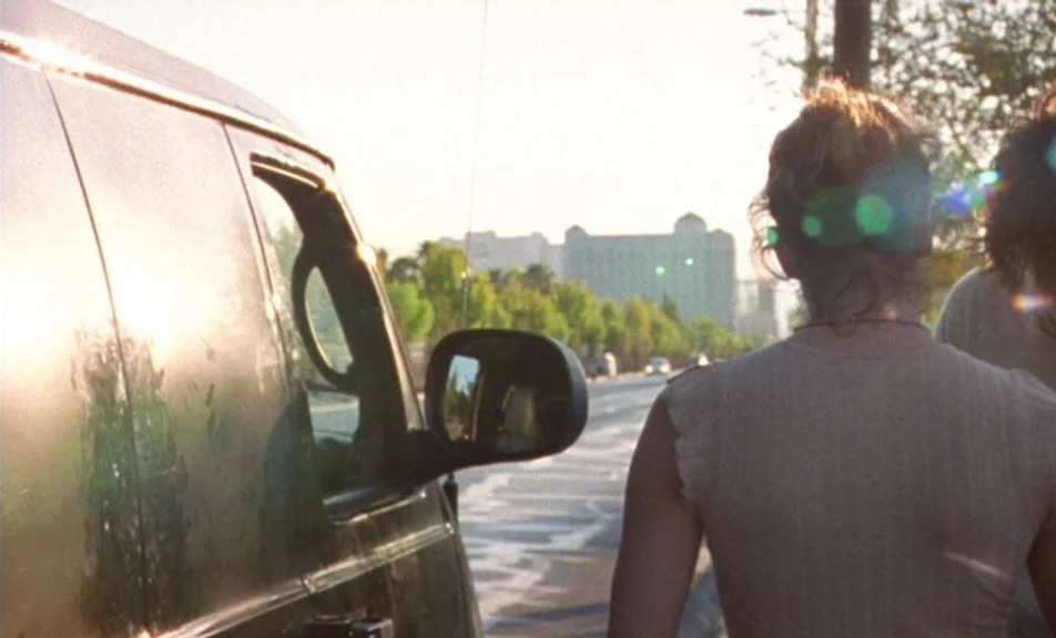 The Brown Bunny (2003) movie still: medium — A sun-drenched suburban road with a van parked in the foreground. Two individuals stand by the vehicle…