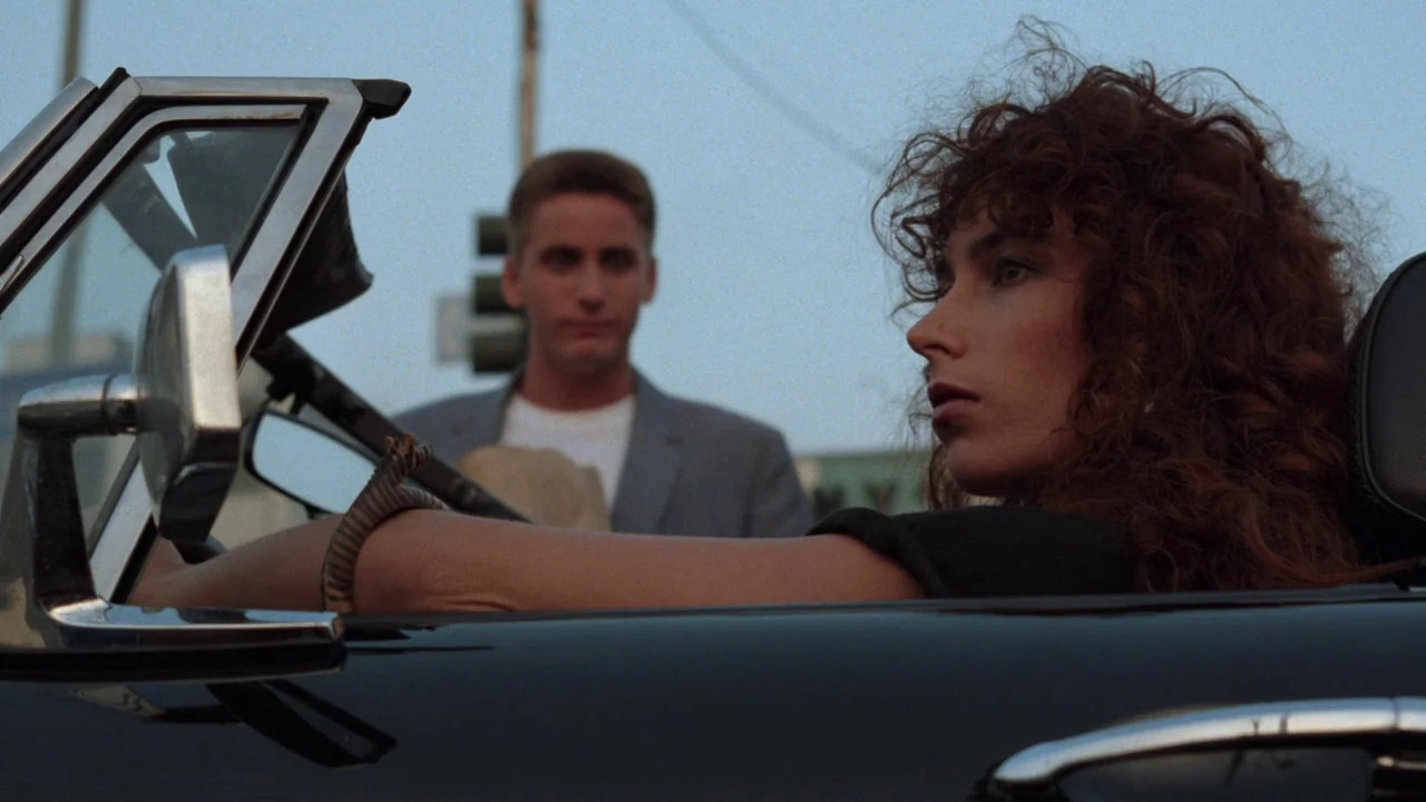 Repo Man (1984) movie still: medium — A woman with red hair sits in a car on a city street. A man in a blazer stands behind her on the street.