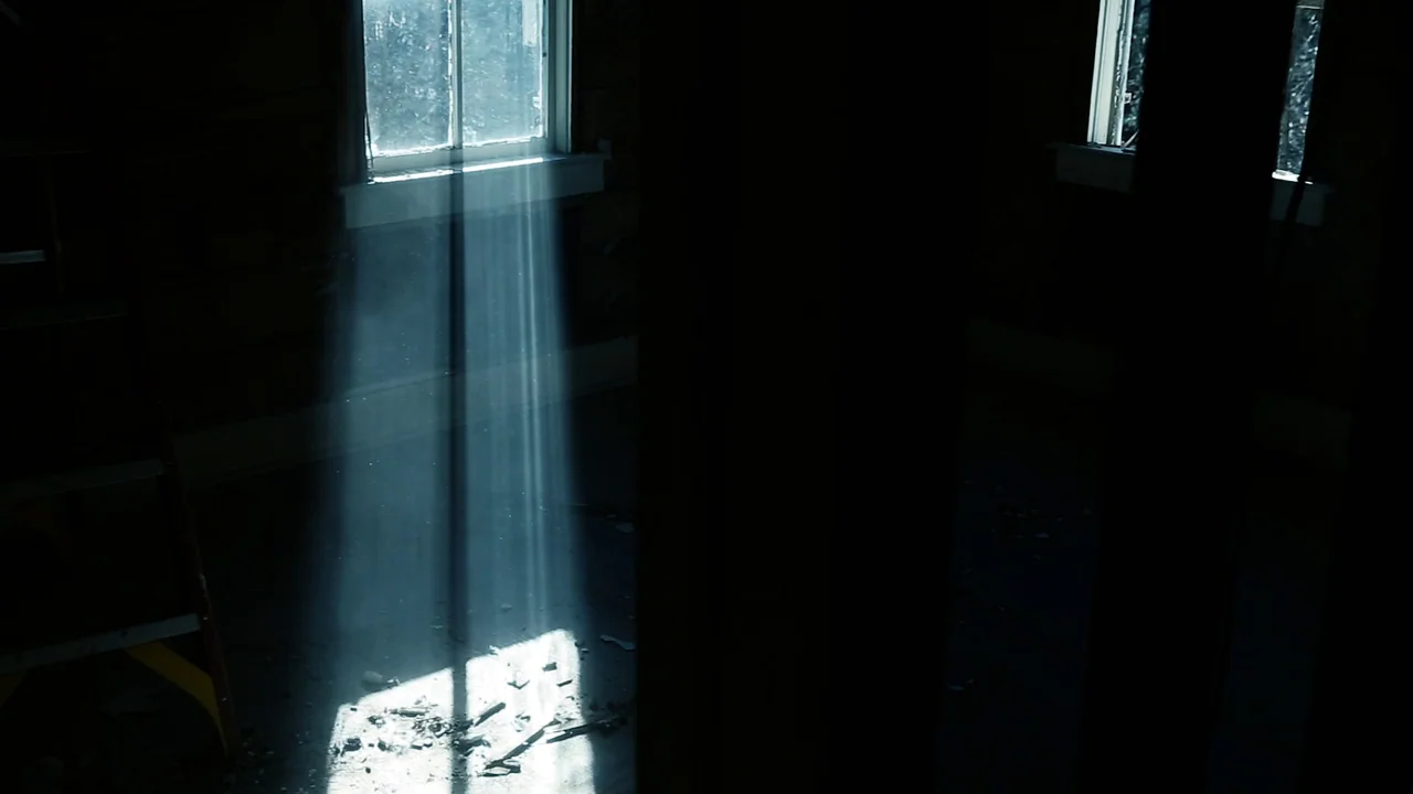 The Deeper You Dig (2019) movie still: establishing — An abandoned, dim room features dark wooden walls and debris scattered on the floor. Sunlight…