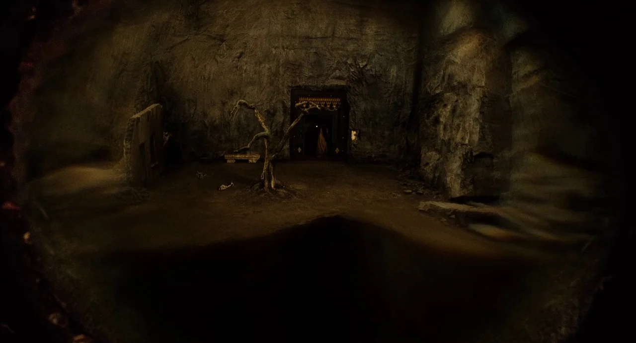 The Immortals (2011) movie still: establishing — A dark, cavernous interior space features jagged stone walls and a single dry tree. An arched…