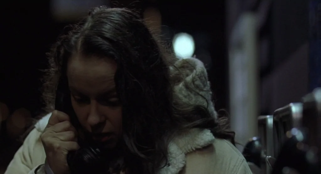 Morvern Callar (2002) movie still: closeup — A woman stands in a dark exterior environment at night near a public phone. She holds a black receiver…