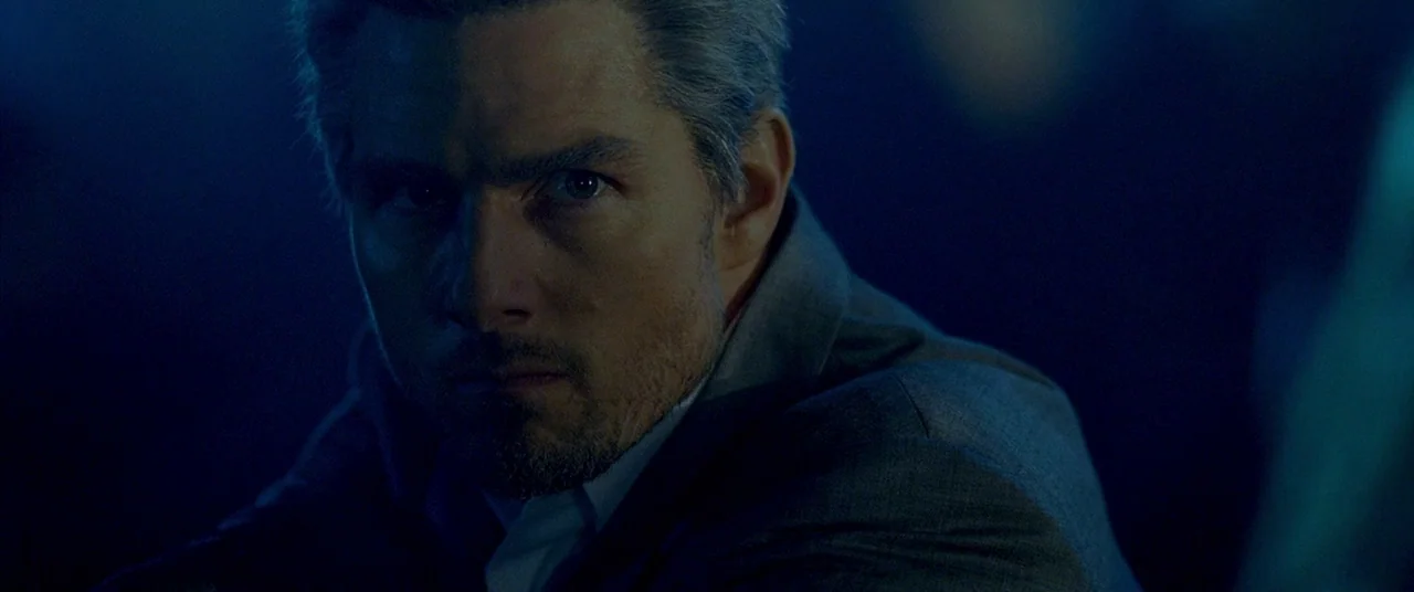 Collateral (2004) movie still: closeup — A man stands in a dimly lit, dark blue environment with minimal visible background detail. The subject…