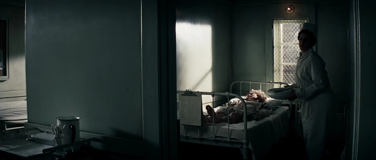 Changeling (2008) movie still: wide — A austere hospital ward features two metal beds separated by a thick structural pillar. A nurse stands by one…
