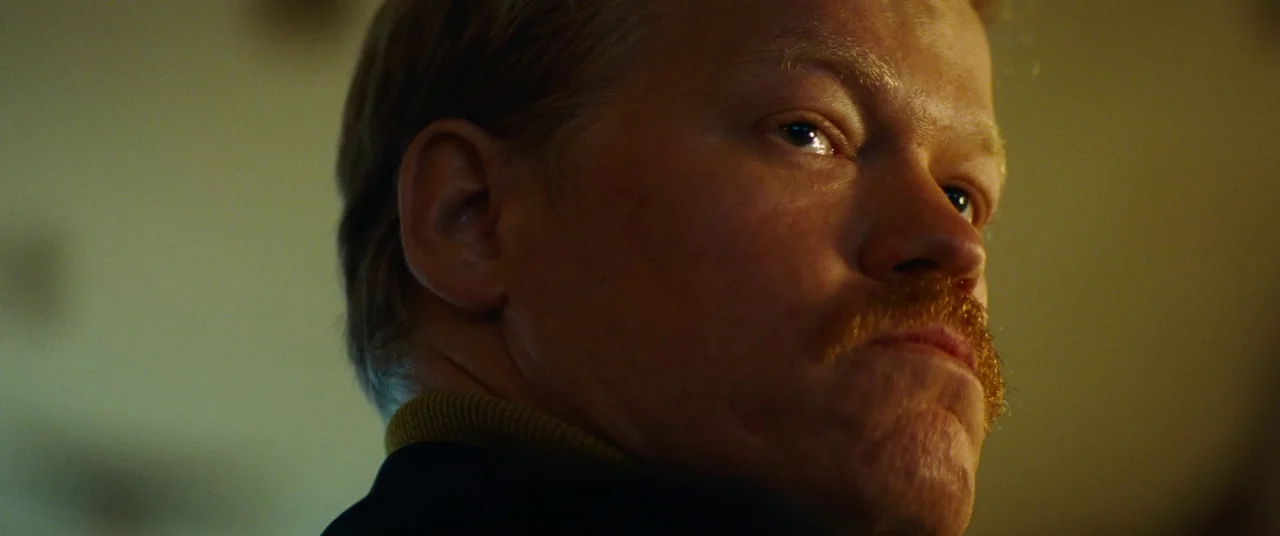 Kinds of Kindness (2024) movie still: closeup — A close-up shot of a man's profile in a dimly lit interior space. The man looks toward the side of…