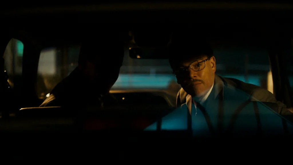 The Informant! (2009) movie still: medium — The interior of a car is cast in deep shadow at night. A man in glasses looks forward from the passenger…