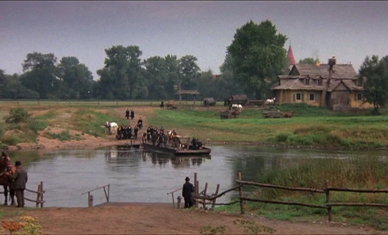 Yentl (1983) movie still: wide — A rural river crossing features a flat-bottomed ferry transporting people and horses across water. A rustic…