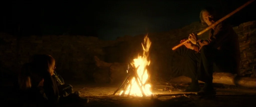 Kill Bill Vol. 2 (2004) movie still: wide — An outdoor campsite at night featuring a stone-lined floor and a small crackling fire. An older man sits…