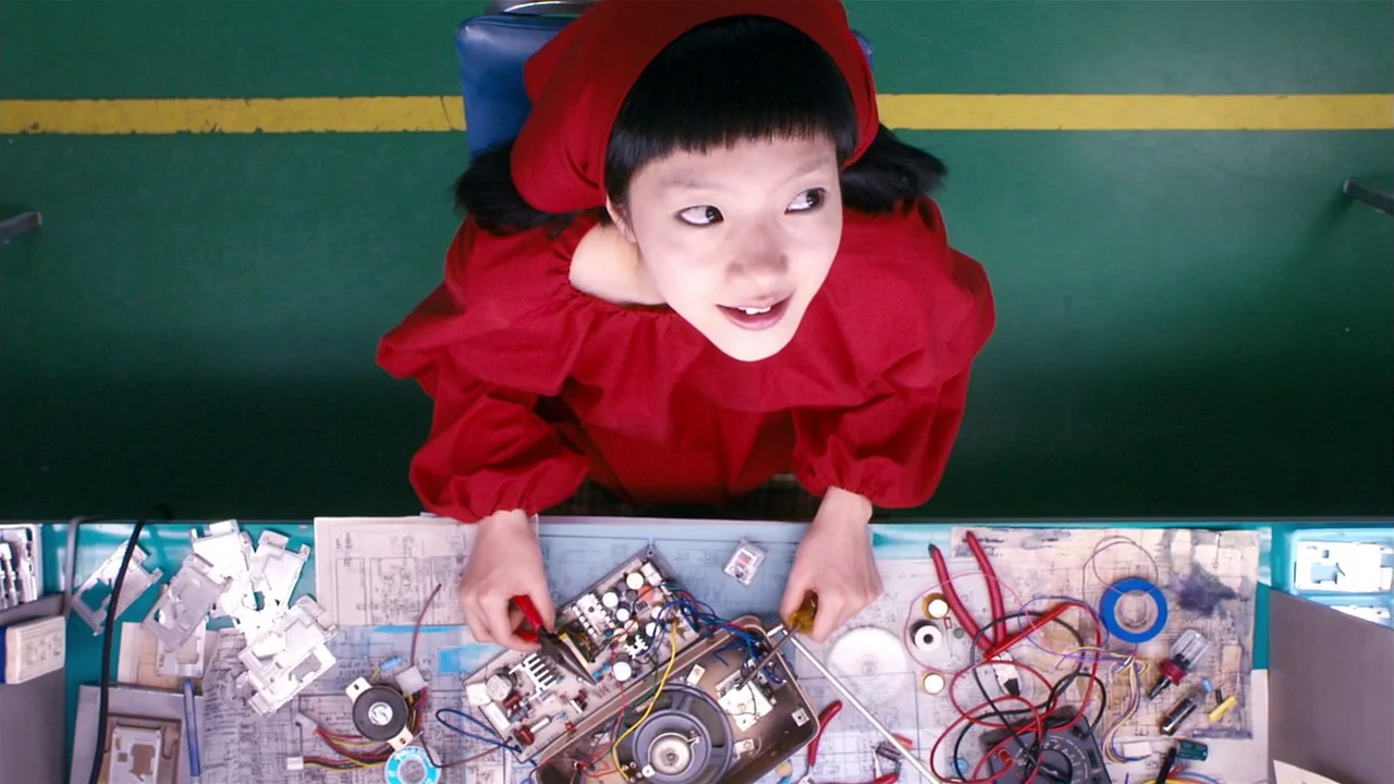 I’m A Cyborg, But That’s Okay (2006) movie still: medium — A green workbench covered in scattered electronic components, wiring diagrams, and metal…