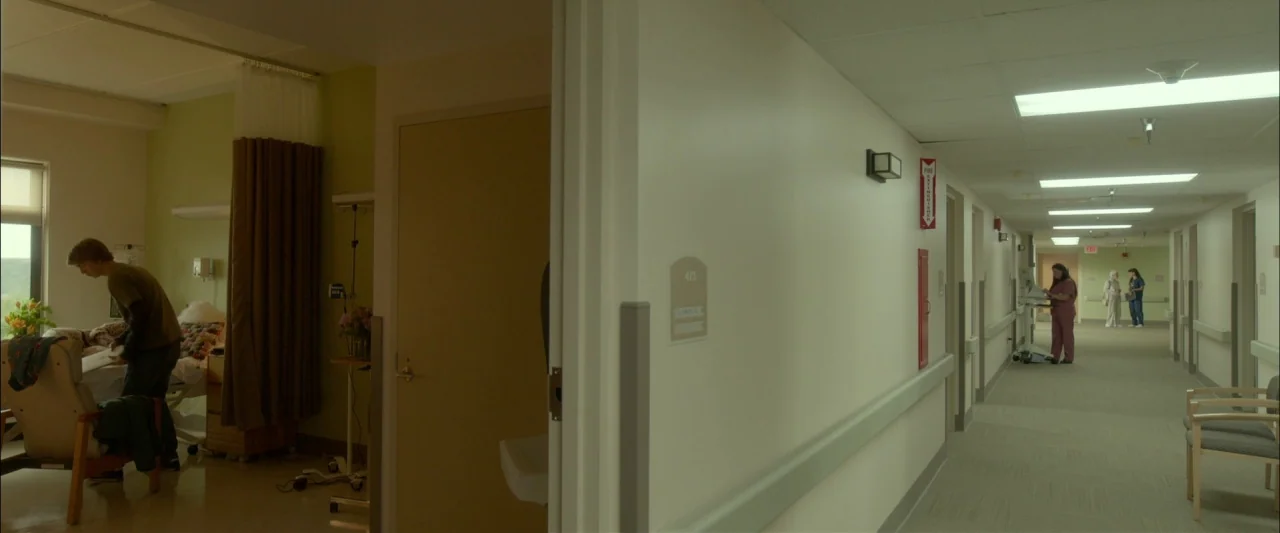 Me and Earl and the Dying Girl (2015) movie still: wide — A hospital wing shows a patient room beside a long, brightly lit clinical hallway. Several…