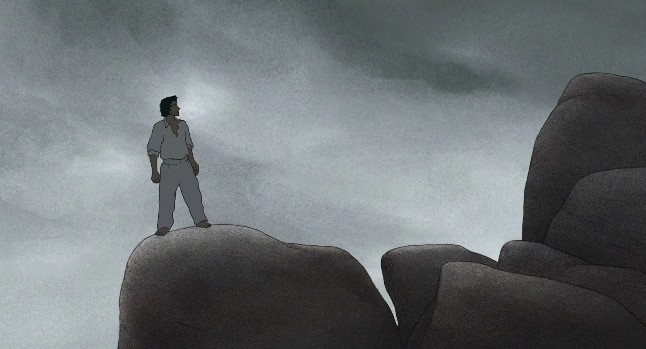 The Red Turtle (2016) movie still: wide — A man stands atop a smooth grey rock against a backdrop of thick clouds. He gazes into the distance from…