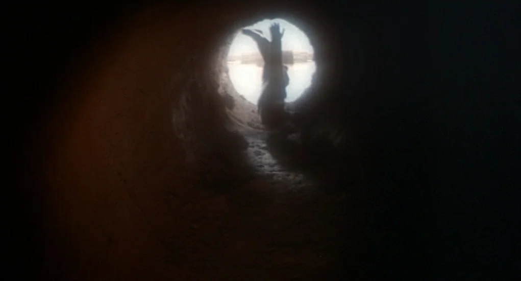 The Other (1972) movie still: wide — A dark concrete tunnel provides a narrow viewpoint toward a bright exterior opening. A person is crawling…