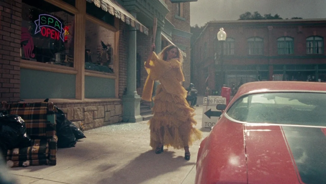 Lemonade (2016) movie still: fullbody — A sidewalk outside a retail storefront with shattered glass strewn across the concrete. A woman in a yellow…