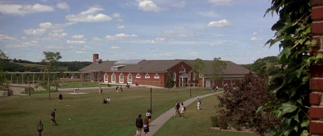 Afterschool (2008) movie still: establishing — A sprawling university campus lawn features a long red brick building with white arched windows.…