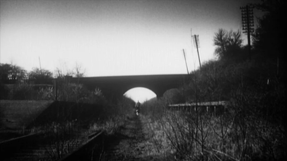 TwentyFourSeven (1997) movie still: wide — A desolate, overgrown set of railway tracks runs toward a distant stone arch bridge. Sparse,…