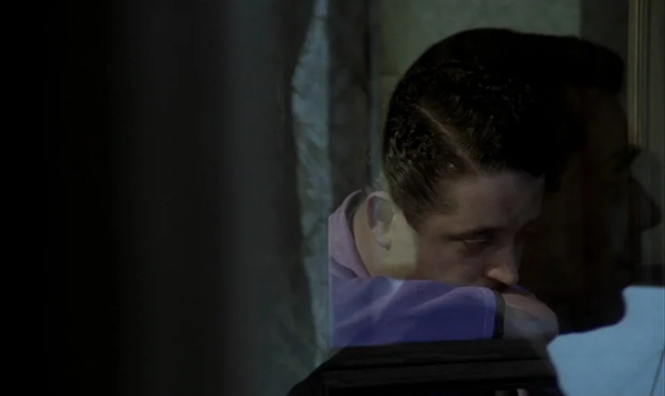 Despair (1978) movie still: closeup — A dimly lit room with heavy shadows casting the surroundings in near darkness. A young man with dark hair…